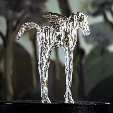 Metallic winged horse figurine on a dark pedestal with a blurred natural background