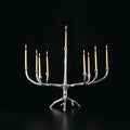 A rustic silver tree-branch style candle holder with nine arms, holding lit yellow taper candles, set against a solid black background.