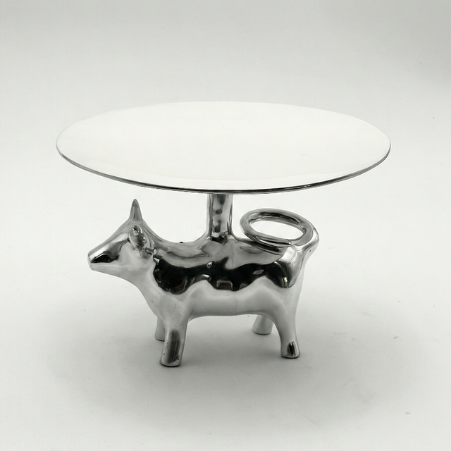 Small round table with a glass top and metallic cow-shaped base on a white background