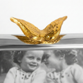 Gold Angelwing figurine on a reflective surface with a black and white photo of two children in the background.