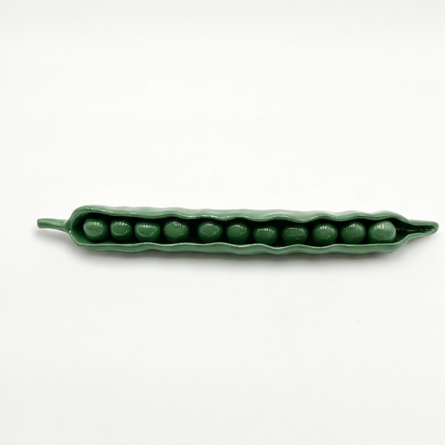 Green ceramic pod with peas on a white background
