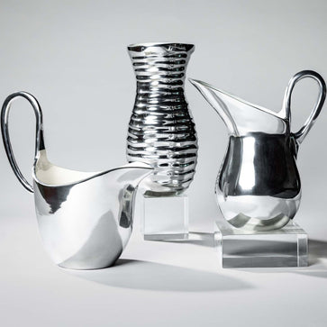 Three silver vases on clear stands against a light gray background